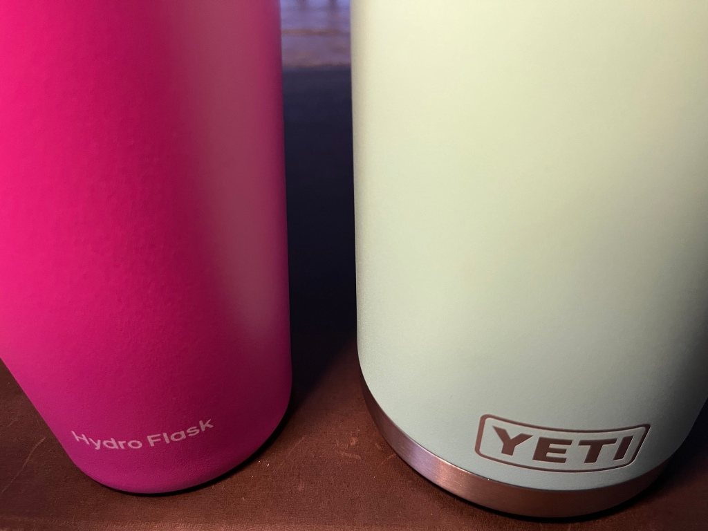 A red hydro flask next to a white yeti bottle